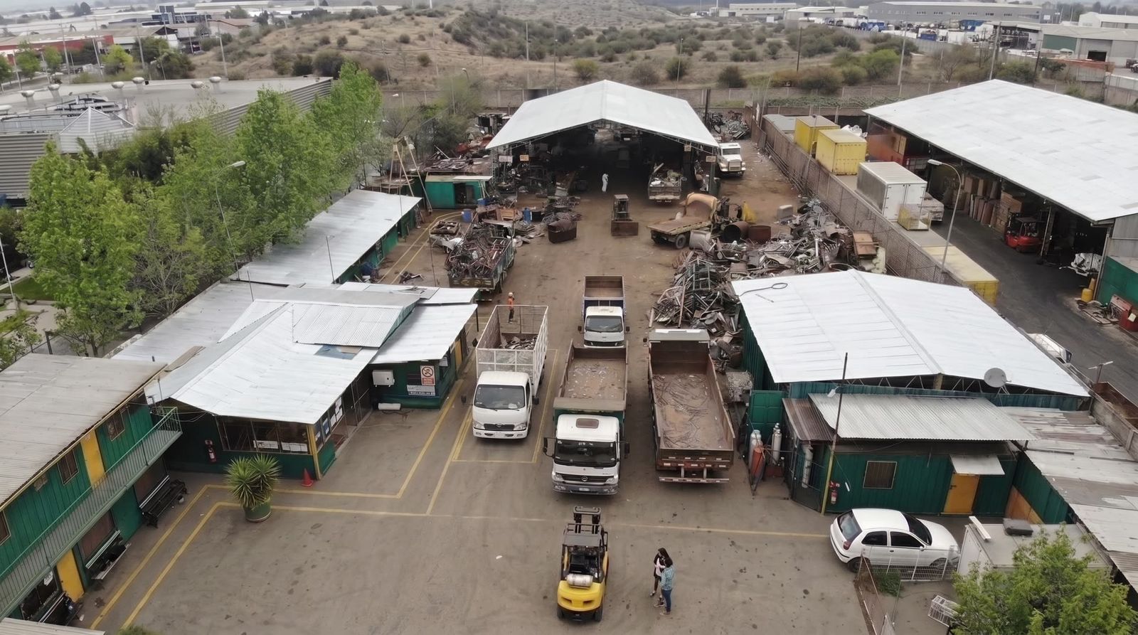 Vista aérea de la planta de Los Maitenes SpA en Quilicura: patio de acopio, galpones techados, camiones cargando y material metálico clasificado.